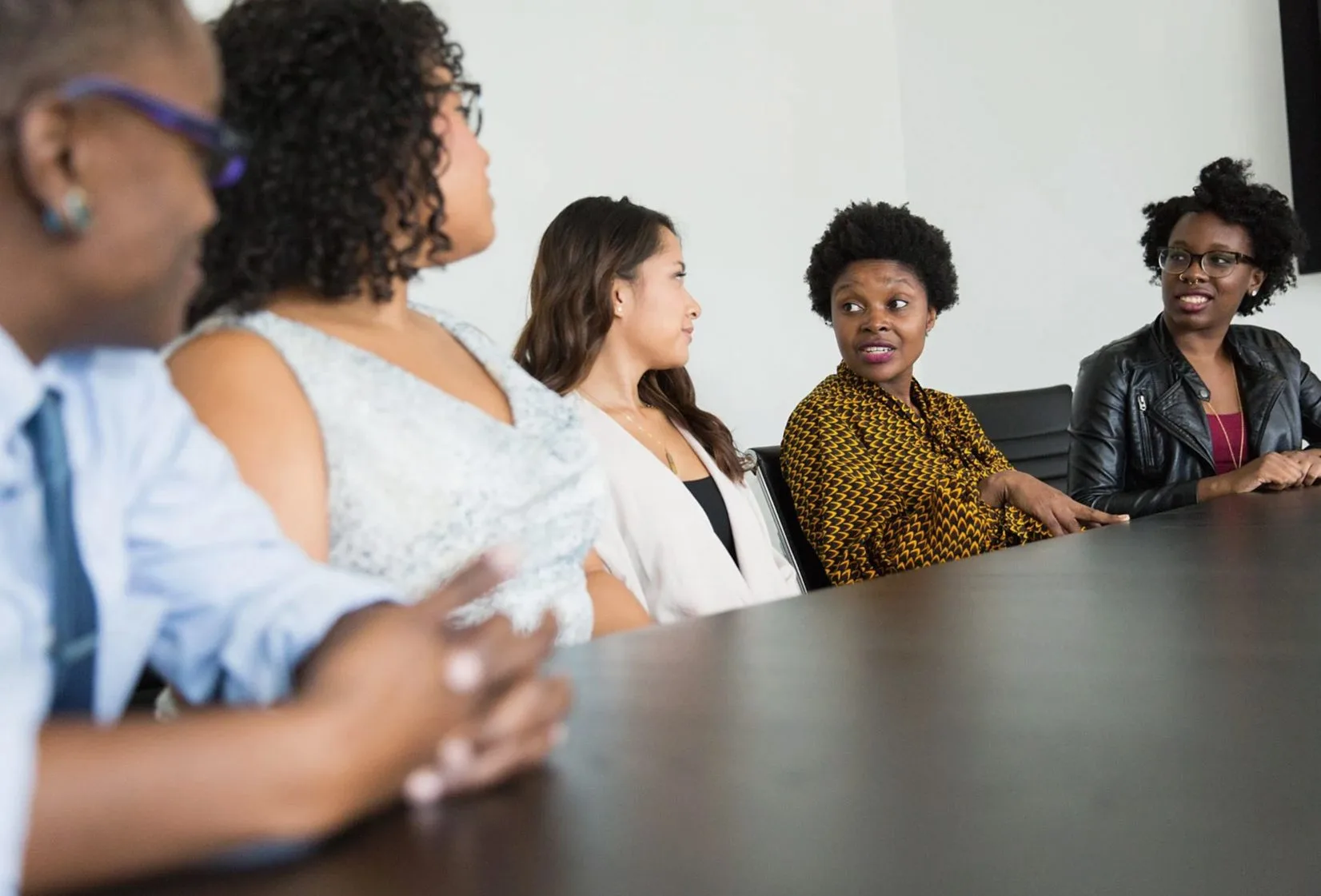 Colleagues sitting along a meeting table, listening to someone speak